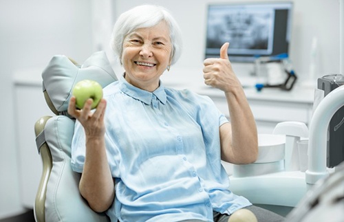 Woman holding an apple while giving a thumbs up and smiling