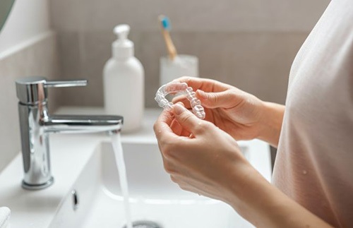 Woman cleaning her Invisalign tray in bathroom