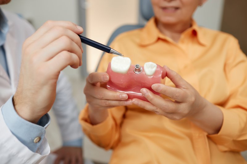 dentist showing mouth mold and dental implant to patient